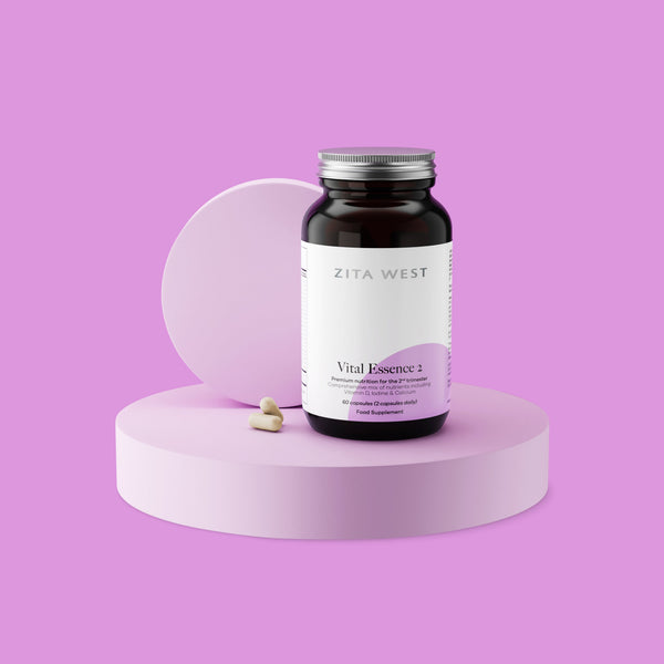 Bottle of Zita West Vital Essence 2 supplement on a purple display with two capsules beside it