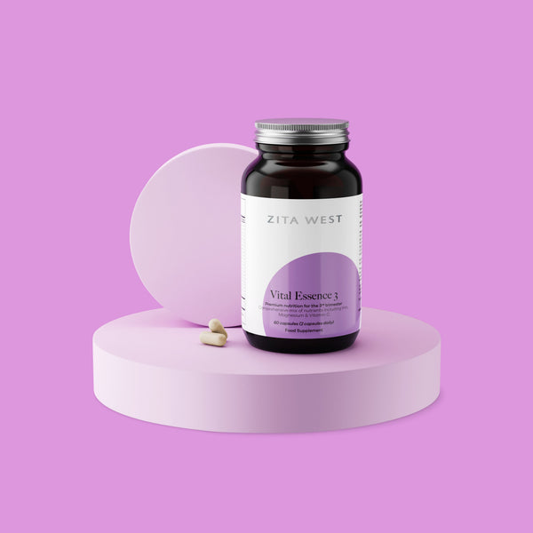 Bottle of Zita West Vital Essence 3 supplement on a purple display with two capsules beside it