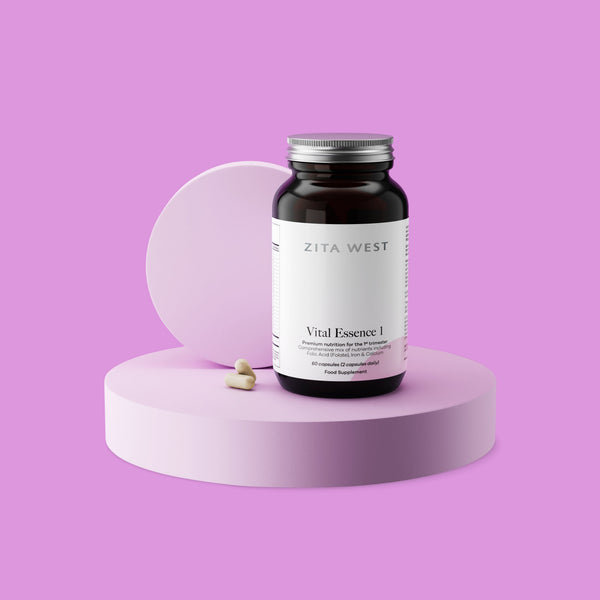 Bottle of Zita West Vital Essence 1 supplement on a pink display with two capsules beside it