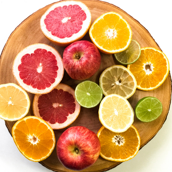 Overhead view of halved citrus fruits and apples arranged on a wooden board