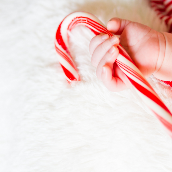 Baby's hand holding a red and white candy cane on a fluffy white blanket
