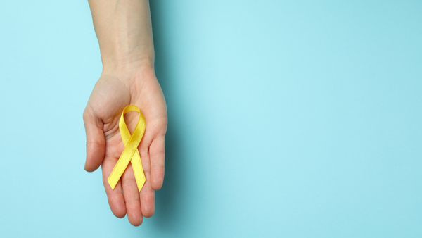 Hand holding a yellow awareness ribbon against a blue background