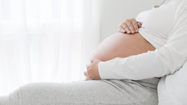 Pregnant woman in white sitting with her hands cradling her belly
