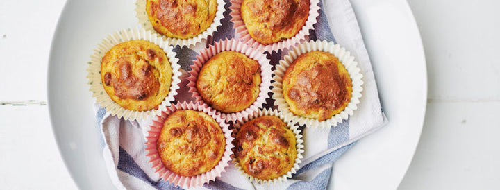 Six golden baked muffins arranged on a plate lined with a striped cloth