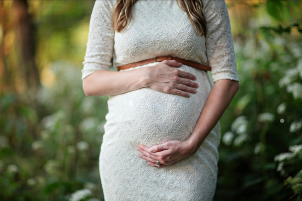 Close-up of a pregnant woman in a lace dress with a hand resting on her belly outdoors