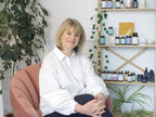 Fertility nutritionist Isabelle Obert seated in a pink chair beside a shelf of Zita West supplements