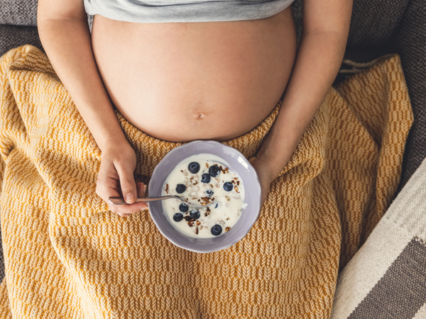 Overhead view of a pregnant woman holding a bowl of yogurt with blueberries and granola