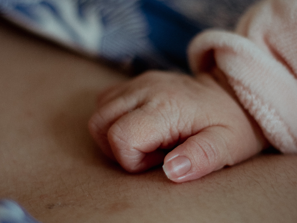 Close-up of a newborn baby's hand resting on a parent's chest
