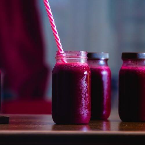 Glass jars of dark beetroot smoothie with a striped straw on a wooden table