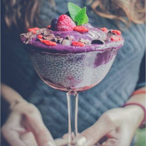 Woman holding a glass of purple berry chia pudding topped with fresh raspberries and mint
