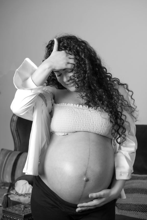 Black and white photo of a pregnant woman with her hand on her forehead looking down at her belly