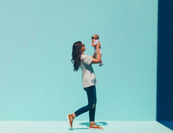 Woman playfully lifting a baby up against a bright blue wall