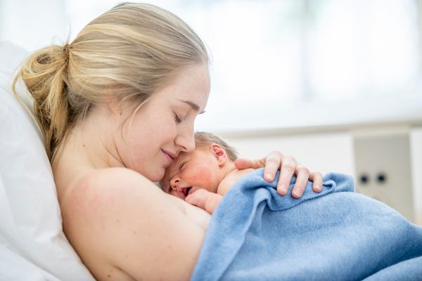 Mother lying skin-to-skin with her newborn wrapped in a blue towel in hospital