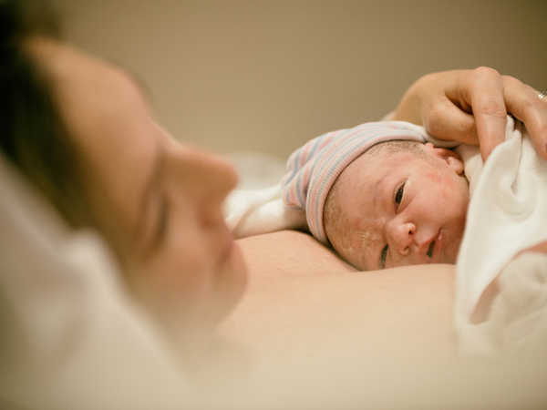 Close-up of a newborn in a striped hat resting on its mother's chest