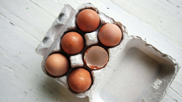 Carton of brown eggs with one cracked shell in the centre