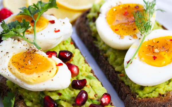 Slices of toast topped with mashed avocado, soft-boiled eggs and pomegranate seeds