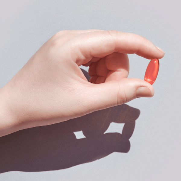A hand holding a red capsule on a neutral background