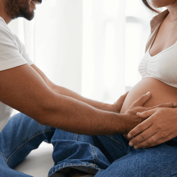 Man's hands resting on his pregnant partner's belly while sitting together