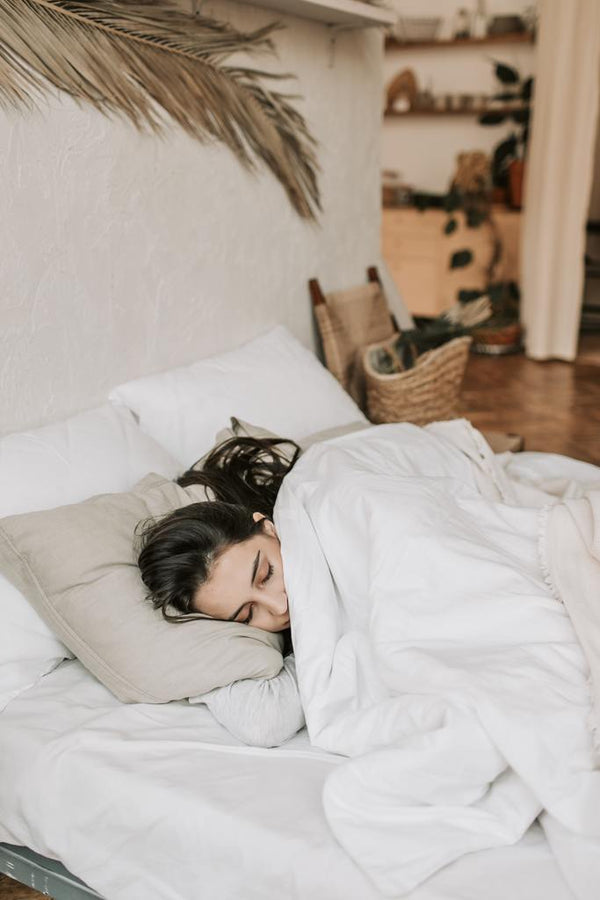 Woman sleeping in bed under a white duvet in a bohemian-style bedroom