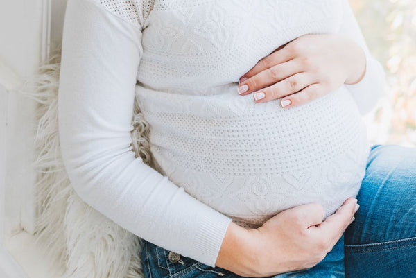 Close-up of a pregnant woman's belly in a white textured sweater with her hands cradling it