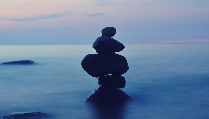 Balanced stack of smooth stones silhouetted against a calm blue sea at dusk
