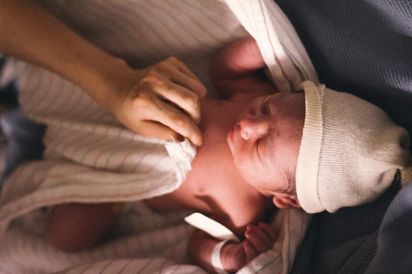 Overhead close-up of a newborn in a knitted hat being gently held by an adult hand