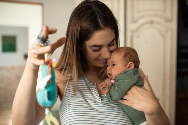 Woman kissing her newborn baby's head while holding a colourful toy