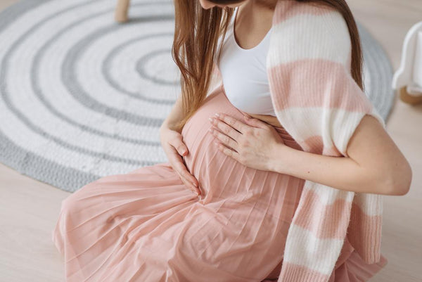 Pregnant woman in a pink dress sitting on the floor cradling her belly with both hands