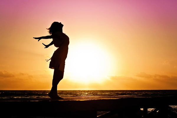 Silhouette of a woman dancing joyfully on a pier at sunset