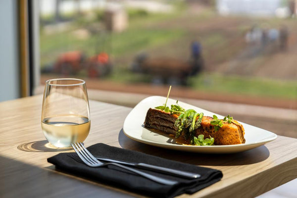 Plated meat dish with asparagus beside a glass of white wine on a restaurant table