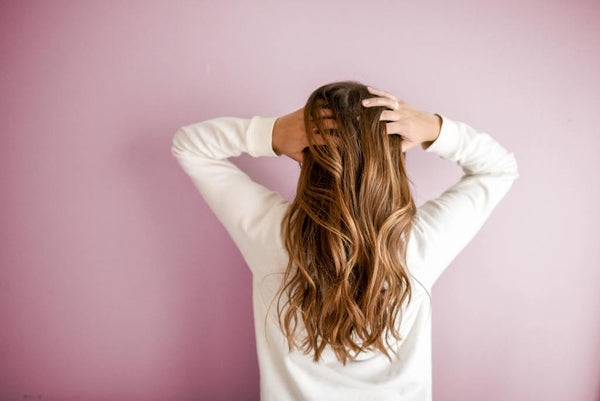 Woman with long wavy hair seen from behind running her hands through her hair