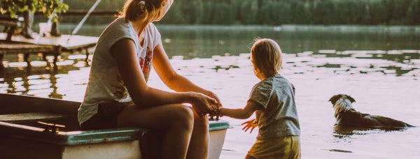 Mother and young child sitting together at the edge of a boat by a calm lake at sunset