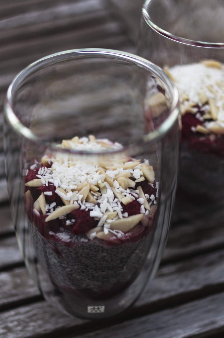 Chia pudding parfaits topped with raspberries, coconut flakes and almond slivers in glass jars