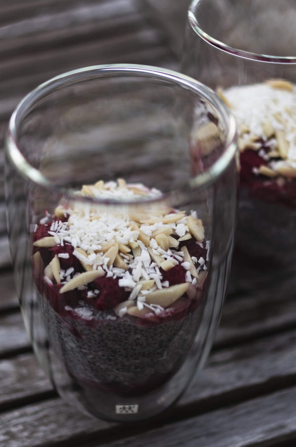 Chia pudding parfaits topped with raspberries, coconut flakes and almond slivers in glass jars