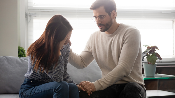 Man comforting a woman sitting beside him on a sofa
