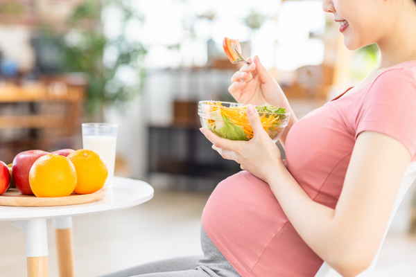 Pregnant woman eating a salad beside a bowl of fresh fruit and a glass of milk