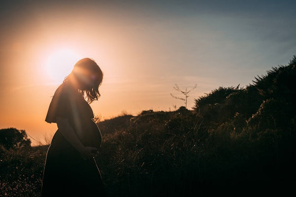 Silhouette of a pregnant woman standing outdoors at sunset