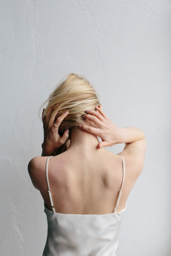 Woman seen from behind in a white slip dress running her hands through her hair