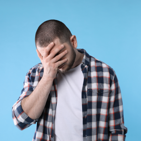 Man covering his face with his hand against a blue background