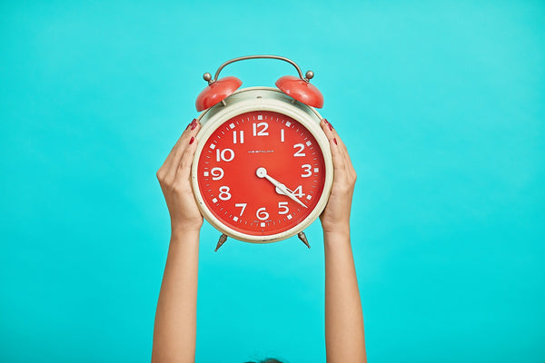 Hands holding up a red alarm clock against a teal background