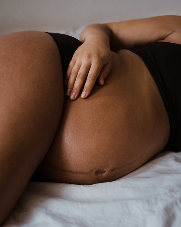 Close-up of a pregnant belly in black underwear with a hand resting on it while lying down