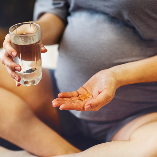 Pregnant woman holding an omega-3 capsule in one hand and a glass of water in the other