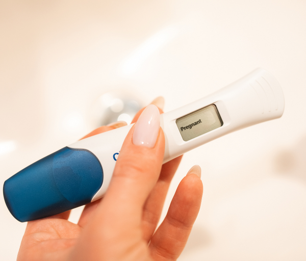 Hand holding a digital pregnancy test displaying the word Pregnant