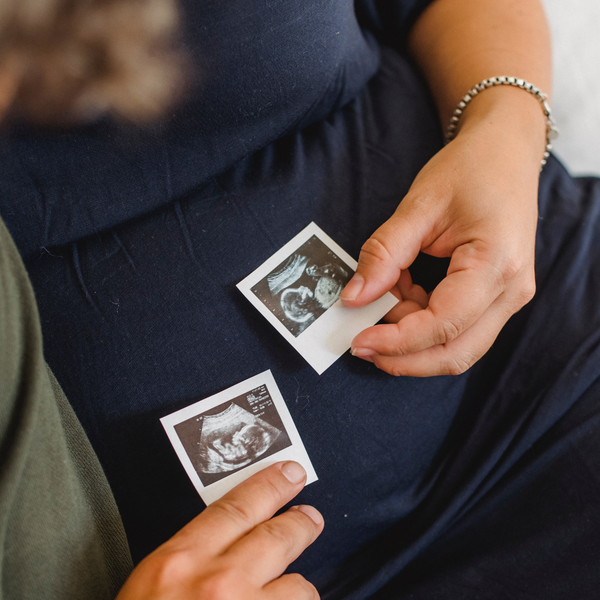 Pregnant woman holding two ultrasound scan photos against her belly