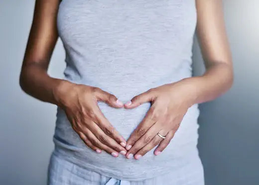 Close-up of a woman's hands forming a heart shape over her stomach