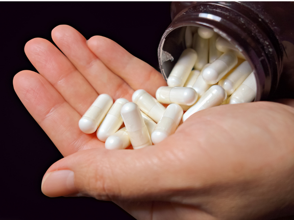 Hand holding a pile of white supplement capsules poured from a bottle
