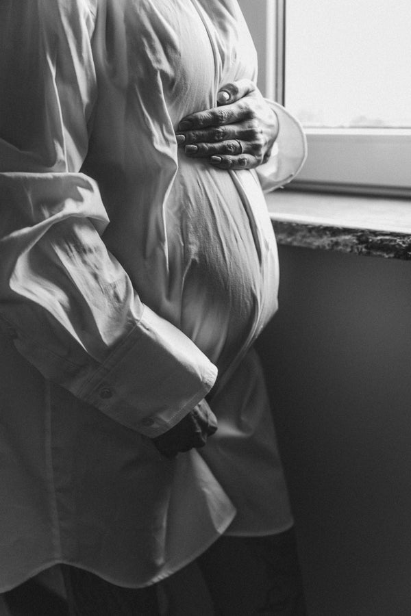 Black and white close-up of a pregnant woman's belly with her hand resting on it by a window