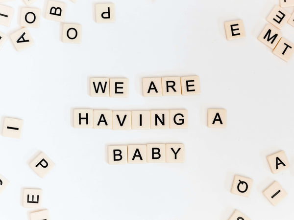 Scrabble tiles spelling out We are having a baby on a white surface