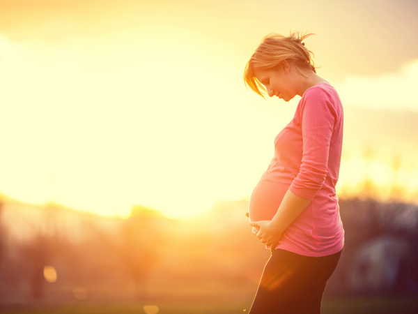 Silhouette of a pregnant woman standing in a sunlit field holding her belly