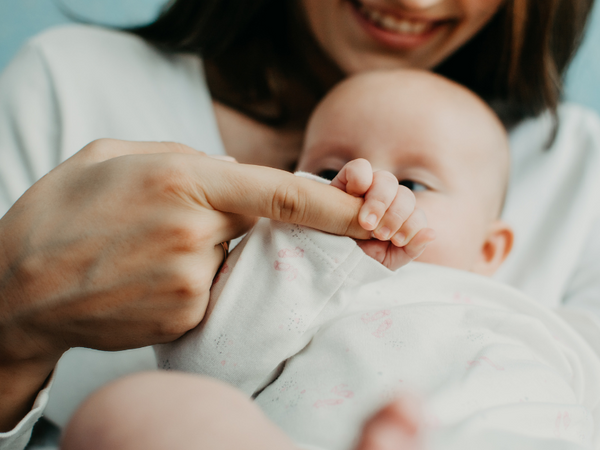 Smiling mother holding her baby's hand close to her chest
